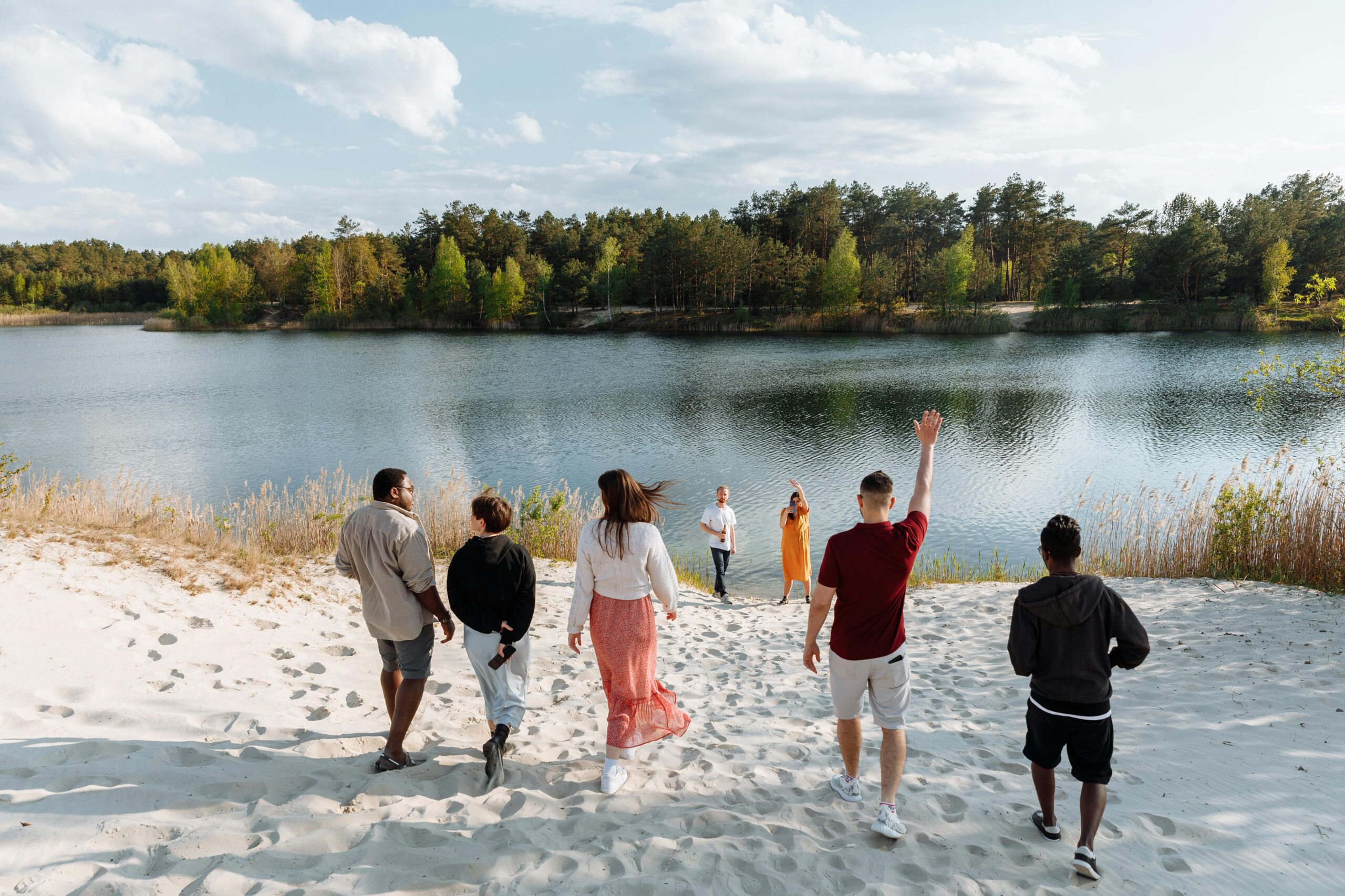 A diverse group of friends walking together towards a serene lake surrounded by lush greenery.